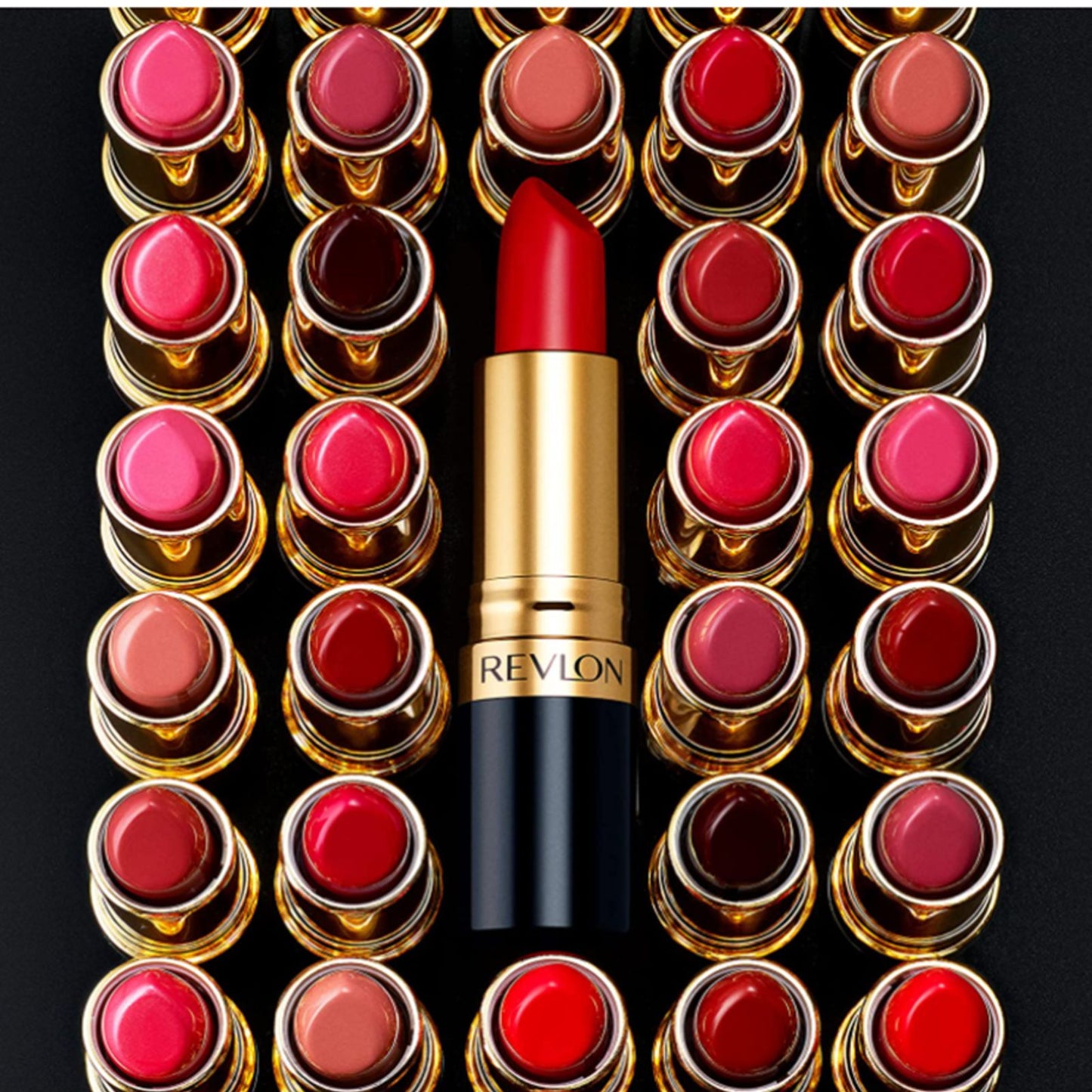 A Revlon lipstick in a bright red shade, centered vertically in front of a grid of multiple lipstick tubes showing various shades, all on a black background.
